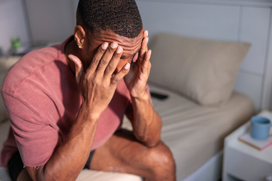 Man in distress, sitting on bed with hands on face.