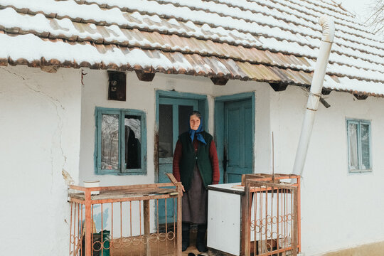 Elderly woman standing at old house doorway in winter