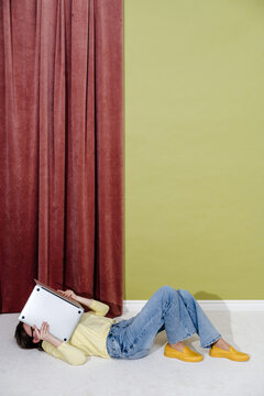 Woman lying on floor and holding laptop above face