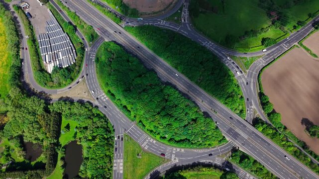 Aerial view of a complex road interchange surrounded by lush green trees and agricultural fields under bright daylight in Hinckley, England, United Kingdom.