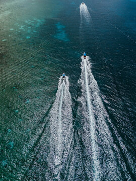Three boats speeding across ocean leaving white wakes
