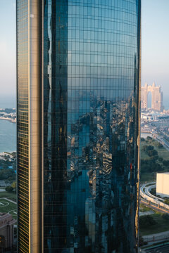Glass skyscraper facade reflecting Abu Dhabi coastline at golden hour