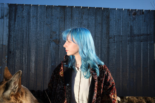 Woman with blue hair stands near a dog by a metal fence