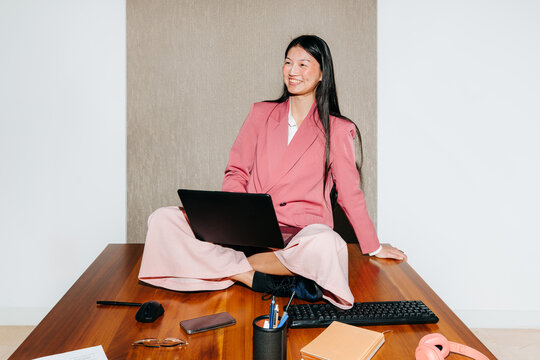 Smiling Woman Sitting on Desk Using Laptop in Modern Office Space