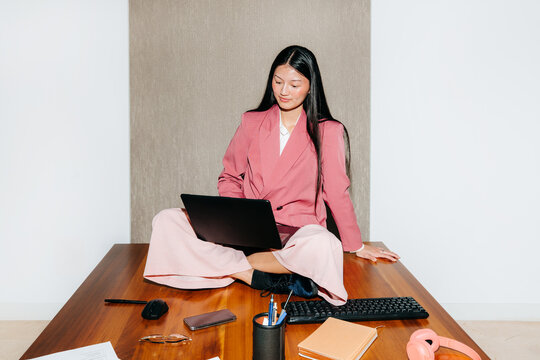 Woman Sitting on Desk Using Laptop in Modern Office Space