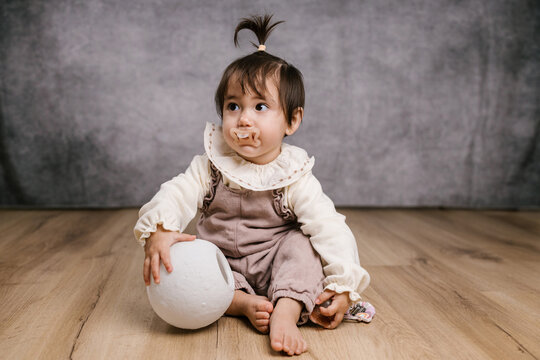 Baby sitting on floor holding white ball