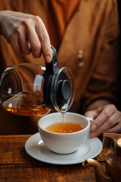 Person pouring hot tea into white teacup 