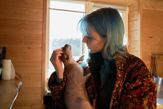 Woman holds a cat inside a wooden cabin with sunlight streaming in
