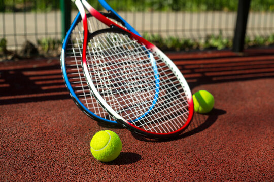 Two tennis rackets and two balls near a bench on a tennis court.