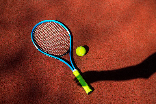Tennis racket and ball with hand's shadow on a tennis court.