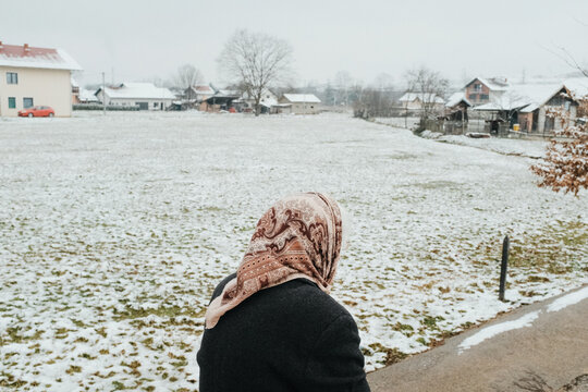 Elderly woman walking beside snowy village field
