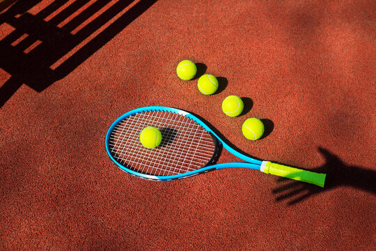 Tennis racket and five balls with hand's shadow on a tennis court.