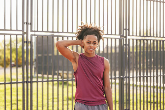 Relaxed young athlete standing by a fence outdoors