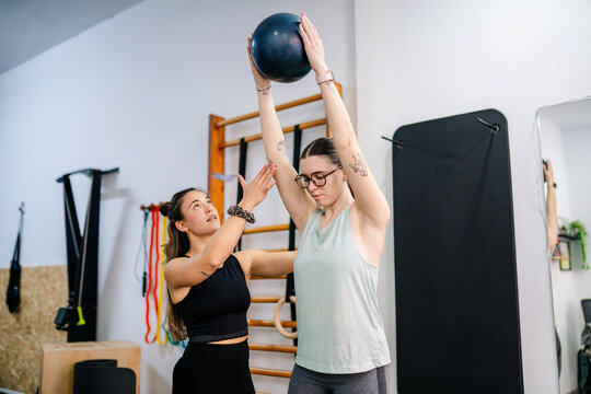 Personal trainer guiding woman lifting medicine ball in gym