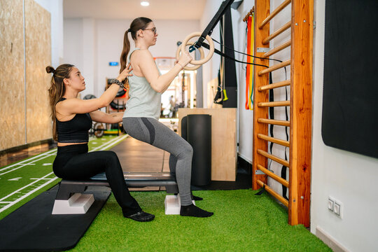 Coach assisting a woman with squats using gymnastic rings