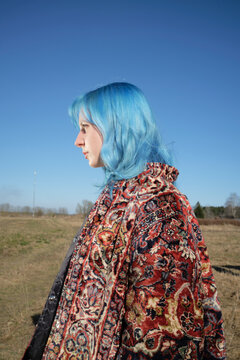 Person with blue hair stands in an open field under clear sky