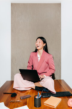 Happy Woman Sitting on Desk Using Laptop in Modern Office Space