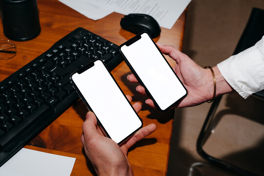 Two Hands Holding Smartphones With White Screen on the Desk