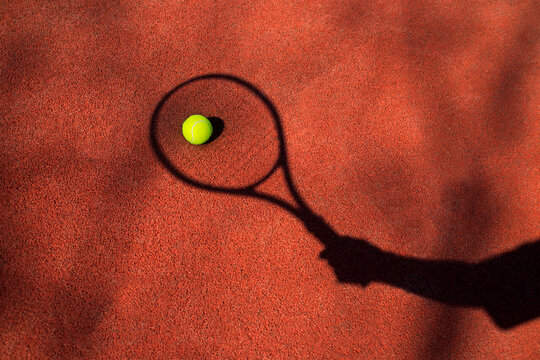 Tennis ball with hand and racket's shadow on a tennis court.