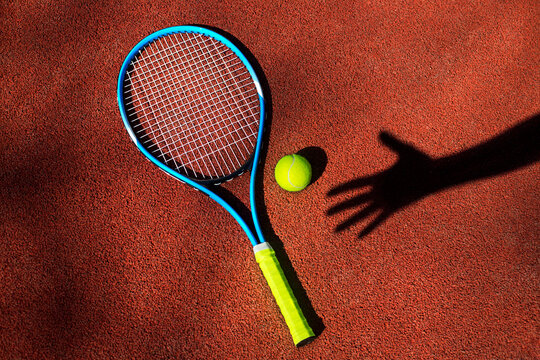 Tennis racket and ball with hand's shadow on a tennis court.