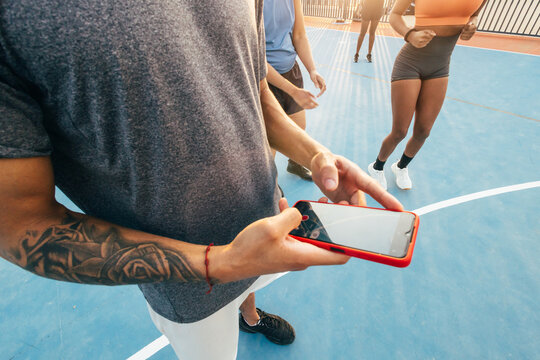 Tattooed person uses smartphone on outdoor basketball court