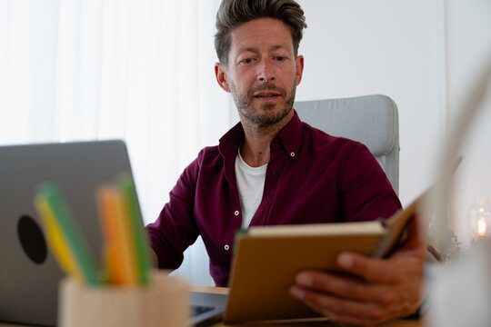 Man Checking Notes While Working on Laptop