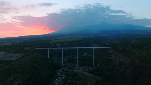 Aerial view of Puente Atenquique I bridge spanning a deep valley with mountains and a colorful sunset sky in the background Atenquique, Jalisco, Mexico.