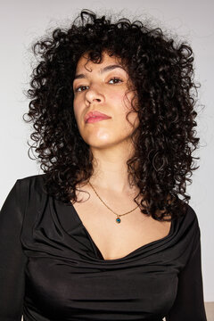 Woman poses with curly hair and simple necklace in studio settin