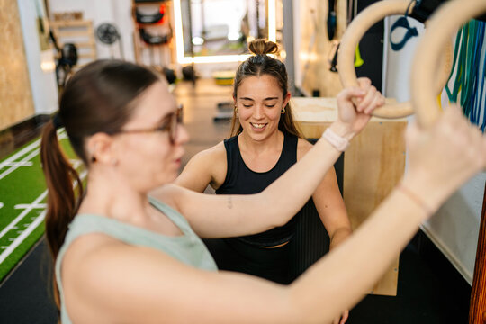 Personal trainer guiding woman using gymnastic rings