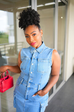 Stylish woman in denim dress holding handbag with confident expression