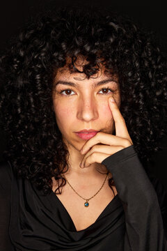 Woman with curly hair poses with finger on chin in studio