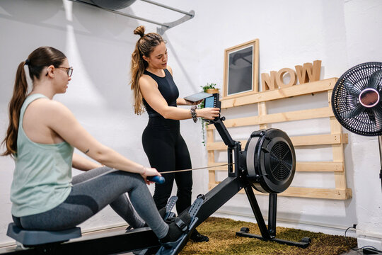 Personal trainer assisting woman with rowing machine workout