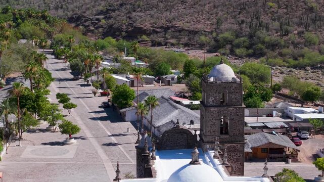 See aerial views of San Javier Mission in Baja California Sur at sunrise. Observe the town and palm trees surrounding the mission