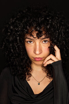 Woman with curly hair looks directly at the camera indoors