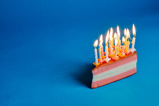 a candle covered cake slice casting a shadow on a blue background