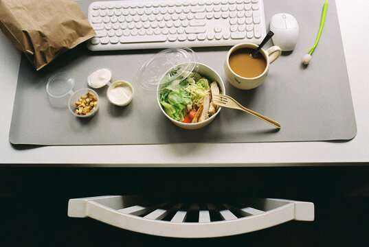 Delivery food on a desk next to a keyboard, computer mouse and pen.