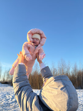 Parent lifts child in snowy field under blue sky