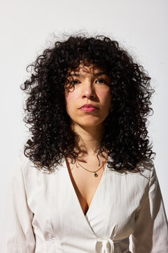 Woman with curly hair stands against white background in studio