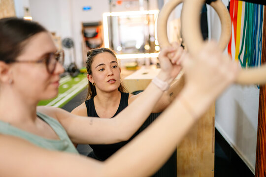 Personal trainer guiding woman on gymnastic rings