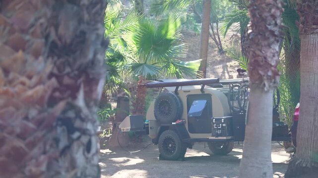 A teardrop camper trailer sits among palm trees in a desert oasis in San Ignacio Baja California Sur Mexico during early morning light
