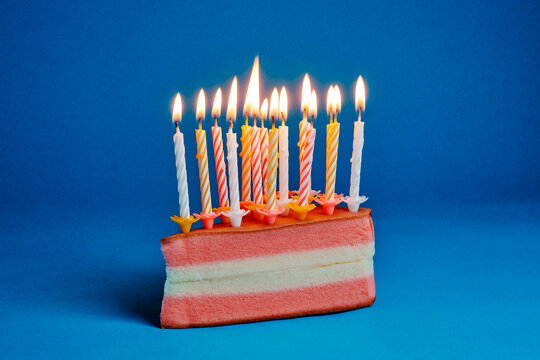 striped birthday candles burning on a pink and white cake slice