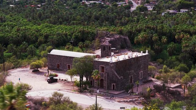 See aerial views of Mission of Santa Rosalia of Mulege surrounded by desert, mountains, and a lush oasis in Baja California Sur.