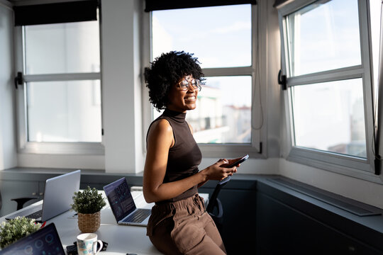Black woman smiling using smartphone in modern office