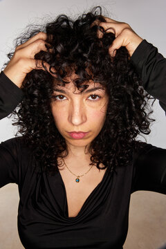 Woman with curly hair looks directly at the camera in studio set