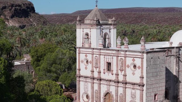 Aerial shots highlight Mission Church in San Ignacio, surrounded by palm trees and desert hills in Baja California, Mexico.