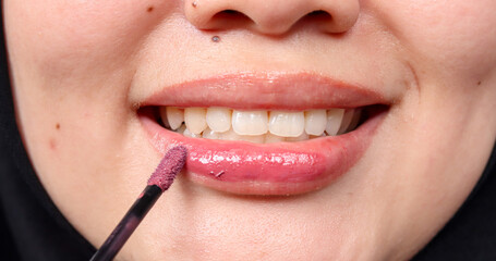 Fototapeta premium Close-up of Asian Muslim woman applying red lipstick, showcasing makeup, beauty routine, cosmetics, and personal care in a lifestyle or fashion setting.