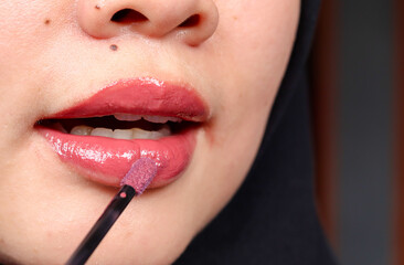 Naklejka premium Close-up of Asian Muslim woman applying red lipstick, showcasing makeup, beauty routine, cosmetics, and personal care in a lifestyle or fashion setting.