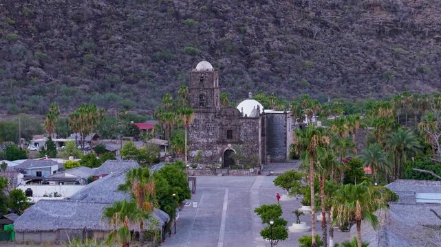 Watch as the sun rises over San Javier Mission in Baja California Sur near Loreto showcasing palm trees and local buildings