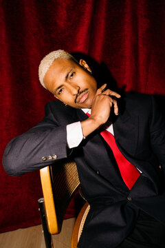 Man in suit sitting against red curtain