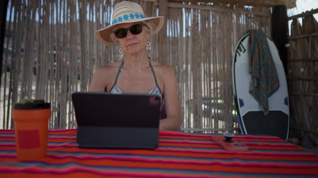 Mature woman shows emotion as she uses computer tablet, and phone on tropical beach during vacation while enjoying the view.